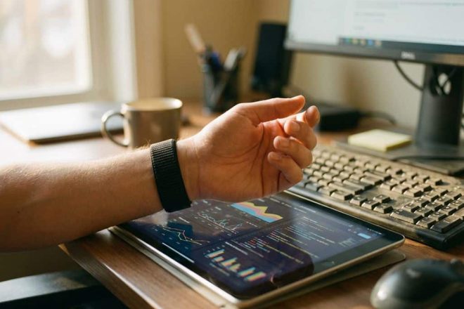 Persoon draagt zwarte RFID-polsband bij tablet met dashboard op kantoorbureau, technologie-integratie