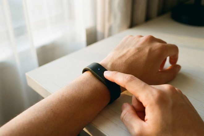 Persoon draagt zwarte RFID polsband met blauwe LED-indicator op moderne bureau in natuurlijk licht